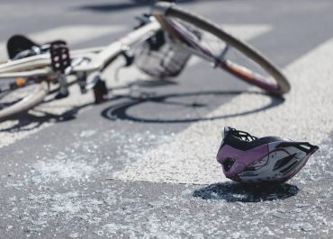 A crashed bicycle on the ground next to shattered glass and a safety helmet.